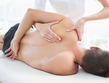 Professional female physiotherapist giving shoulder massage to man in hospital